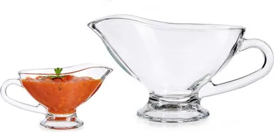 Two glass gravy boats on a white background. One is filled with sauce and garnished with a sprig of parsley, the other is empty.