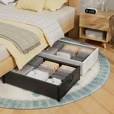 Under-bed storage boxes filled with folded clothes are shown next to a bed.