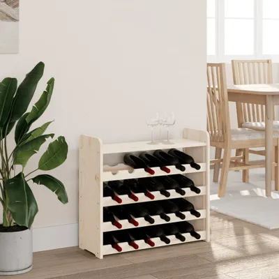 A wooden wine rack filled with red wine bottles is placed next to a large potted plant in a room with a dining table and chairs in the background.
