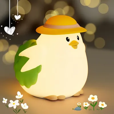 A cute, glowing silicone chick night light wearing a yellow hat, sitting on a surface with small white flowers and a rock.