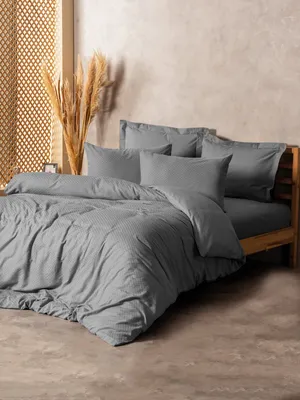 A neatly made bed with grey bedding and pillows, set against a textured wall and a decorative screen.