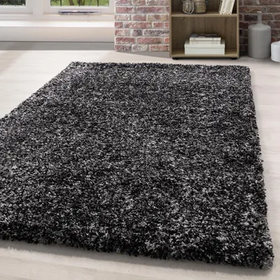 A shaggy rug is shown on a light-colored wooden floor in a room with a brick wall and a bookshelf in the background.