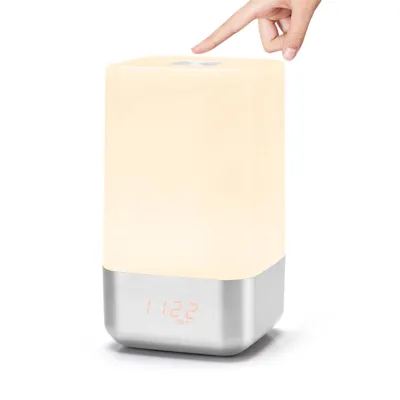 A hand is touching the top of a bedside lamp with a digital clock display.