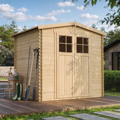 A wooden garden shed with tools and boots leaning against it, set on a wooden deck with grass and paving stones in the foreground.