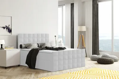 A white upholstered bed with a headboard and storage drawers in a bright, modern bedroom setting.