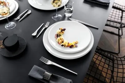 A beautifully set dining table with white plates, silverware, and wine glasses, suggesting a formal dining experience.