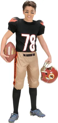 A young boy dressed in an American football costume, holding a football and a helmet.