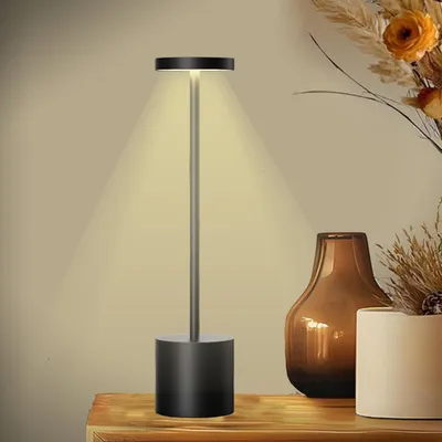 A modern, minimalist table lamp with a black base and a silver stem, casting a warm light.
