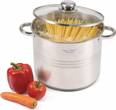 A stainless steel pot filled with spaghetti, with a glass lid slightly ajar, sits next to a red bell pepper, a tomato, and a carrot on a white background.