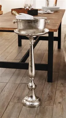 A silver decorative stand holding a champagne bucket on a wooden table.