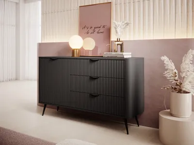 A dark gray dresser with fluted drawers and doors is placed in a modern room with pink and cream walls. Decorative items like lamps and a framed picture are on top of the dresser.