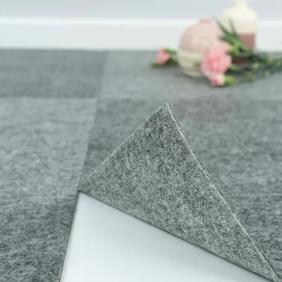 A close-up of grey carpet tiles, with one tile lifted to show the adhesive backing.