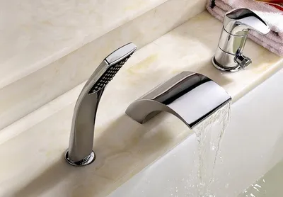 A modern chrome bathtub faucet set with a waterfall spout and a handheld showerhead, installed on a marble countertop.