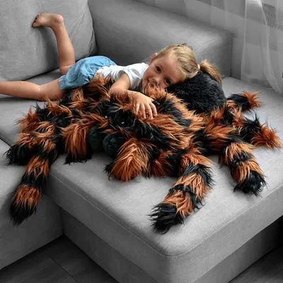 A young girl is lying on a sofa with a large plush spider toy.
