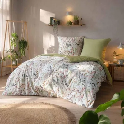A bedroom scene with a bed dressed in floral bedding, plants, and natural light.