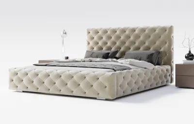 A tufted beige bed with pillows and a bedside table with a lamp and vase.