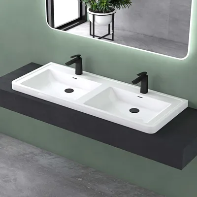 A modern double sink bathroom vanity with black faucets, set against a green wall and a concrete floor. A mirror reflects a potted plant.