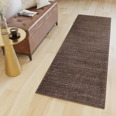 A runner rug is placed on a light-colored wooden floor next to a brown leather storage bench and a gold side table.