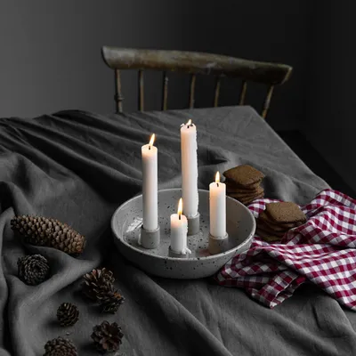 A table setting with lit candles, pinecones, and cookies, suggesting a cozy, festive atmosphere.
