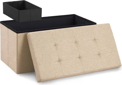 A beige storage ottoman with its lid open, revealing a black interior and a black insert box on top. The lid is tufted with buttons.