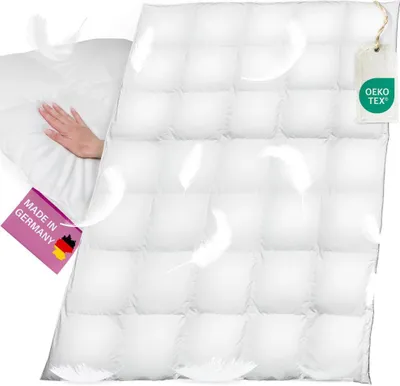 A white down comforter is shown with a hand pressing into it, and feathers floating around. There are two tags attached to the comforter.