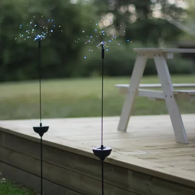 Two solar-powered garden lights shaped like starbursts are placed on a wooden deck next to a picnic table.