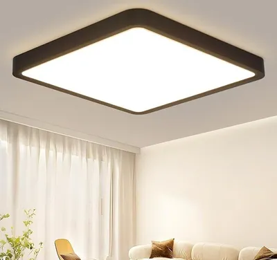 A square LED ceiling light is mounted on a white ceiling above a sofa and curtains.
