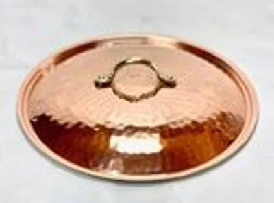 A copper pot lid with a handle is shown on a light-colored surface.