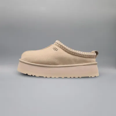 A single beige UGG slipper is shown from the side against a plain gray background.