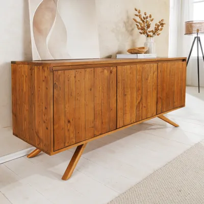A wooden sideboard in a room with a painting and dried flowers.