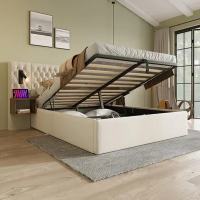 A bedroom scene with a bed that has its storage compartment open, revealing the mattress and slatted base. A small bedside table with a lamp and tablet is attached to the headboard. Artwork hangs on the wall above the bed.