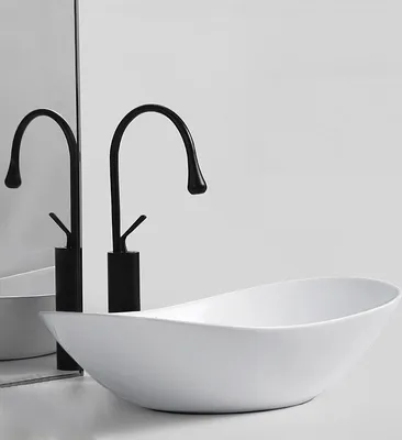A white oval washbasin with two black faucets in front of a mirrored background.