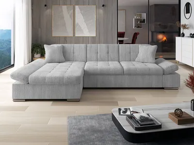 A light gray sectional sofa is displayed in a modern living room setting with a large window and artwork on the wall.