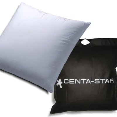 A white pillow is placed next to a black bag with the brand logo and name on it.