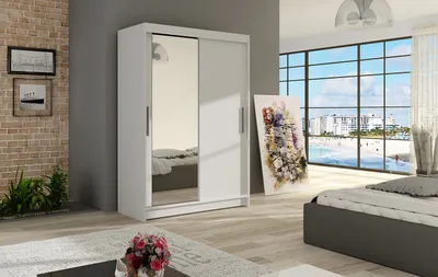 A modern bedroom with a white sliding door wardrobe with a mirrored door, a bed, and a large window overlooking a beach.