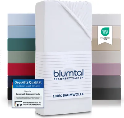 A stack of colorful fitted sheets and a white fitted sheet with branding and certifications.