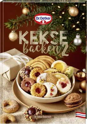 A festive arrangement of Christmas cookies and a gift box, with a decorated Christmas tree in the background.