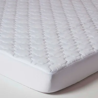 A close-up, angled view of a white quilted mattress topper on a white mattress.