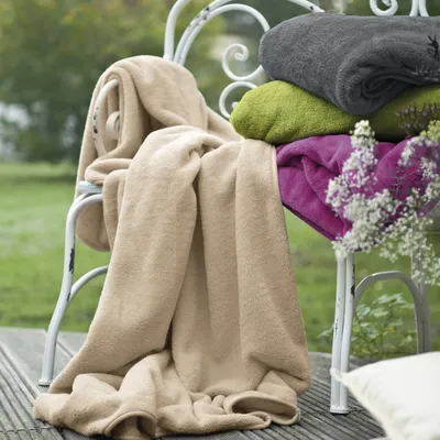 Several folded blankets are stacked on a white chair outdoors, with a wooden deck in the foreground and greenery in the background.