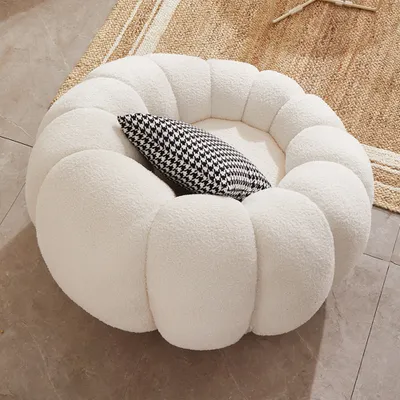 A fluffy white round chair with a black and white patterned pillow inside, placed on a rug and floor.