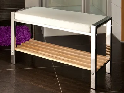 A white upholstered bench with a wooden slatted shelf underneath, placed on a dark tiled floor.
