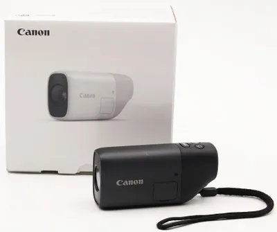 A black Canon PowerShot Zoom camera is in the foreground, with its white packaging in the background.