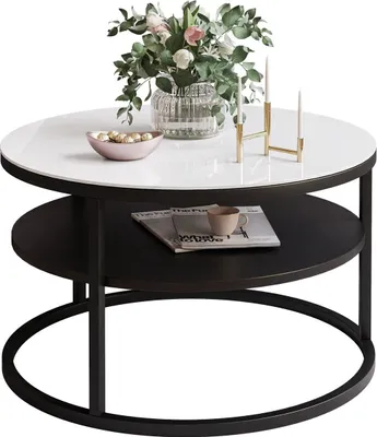 A round coffee table with a white top and black shelf, decorated with a vase of flowers, a bowl of candies, and a candle holder.