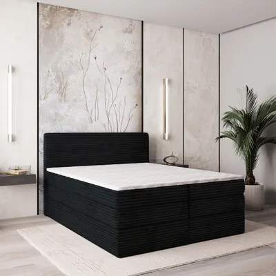 A black boxspring bed with a white mattress and topper is shown in a bedroom setting with decorative wall panels and a plant.