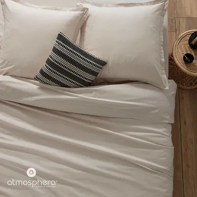 A close-up view of a bed with beige bedding and a decorative pillow.