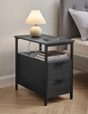A bedside table with a lamp, books, and a phone, next to a bed.