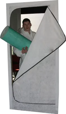 A man in a white protective suit holds a green roll of material inside a white zippered dust protection door.