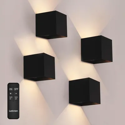 Four black cube-shaped wall lights mounted on a white wall, with light beams projecting upwards and downwards.