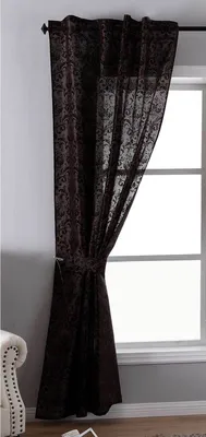 A brown patterned curtain is tied back with a tie-back and hangs next to a window.