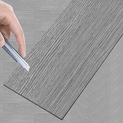 A hand is shown cutting a piece of vinyl flooring with a utility knife.